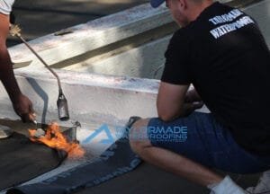 Director from TaylorMade Waterproofing inspecting the torch‑on membrane installation on a flat roof.
