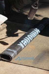 Close up of torch‑on waterproofing membrane being heated and fused to surface during installation.