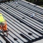 TM Waterproofing painting a corrugated roof with protective coating for durability and weather resistance.
