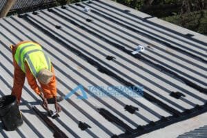 TM Waterproofing painting a corrugated roof with protective coating for durability and weather resistance.