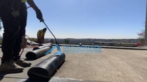 TM Waterproofing applying a torch‑on waterproofing membrane; close view of one technician holding the torch during application.