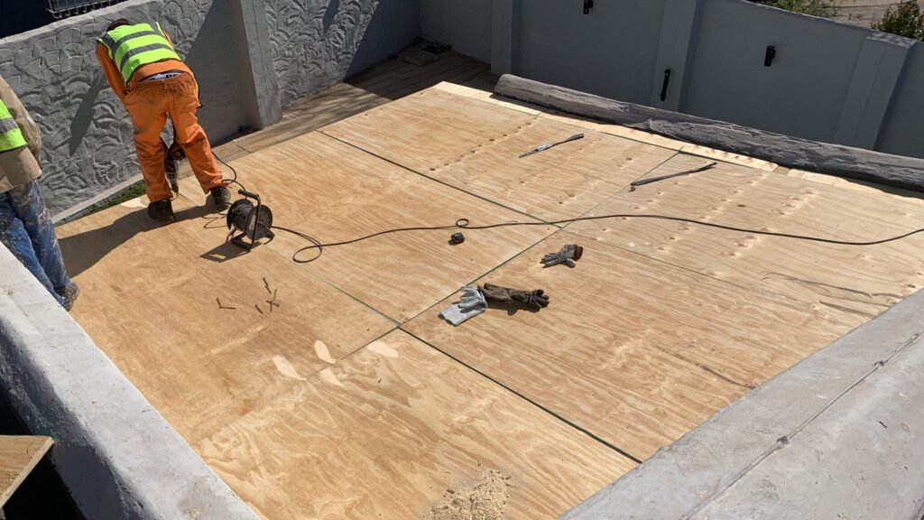 TM Waterproofing installing boards on a flat roof with drills, preparing the surface for Board & Torch Waterproofing.