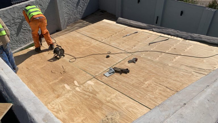 TM Waterproofing installing boards on a flat roof with drills, preparing the surface for Board & Torch Waterproofing.