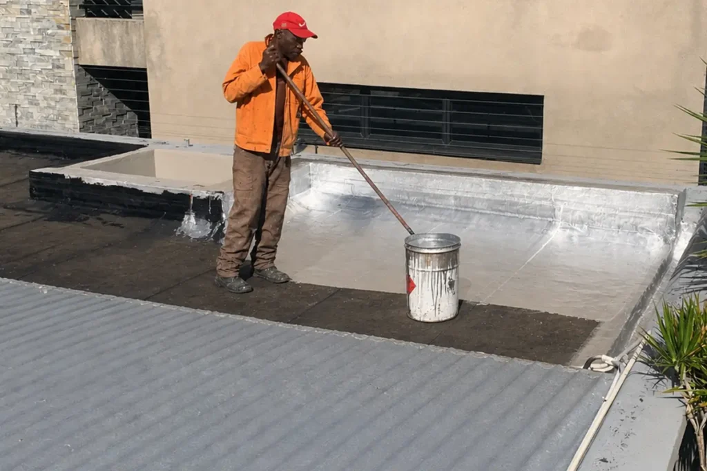 Flat roof waterproofing Parkhurst worker applying silver protective coating over torch-on membrane