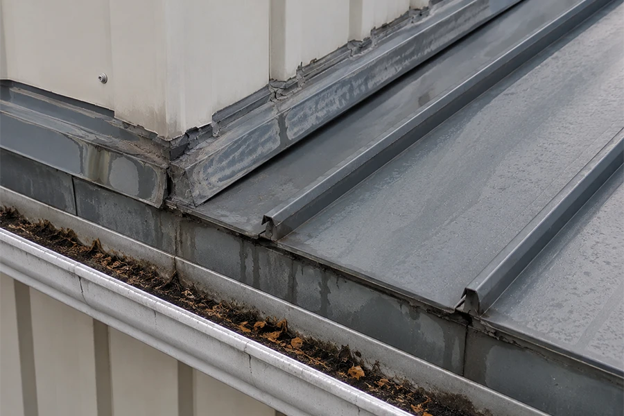 Metal roof waterproofing Johannesburg image showing blocked gutter, wall junction and metal roof edge where leaks can start