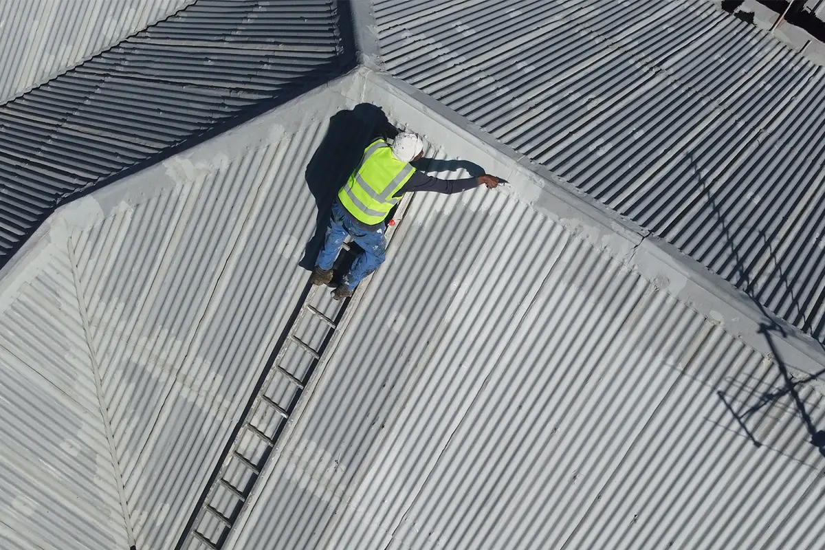 Metal roof waterproofing Westcliff worker applying coating from a ladder on the upper roof section