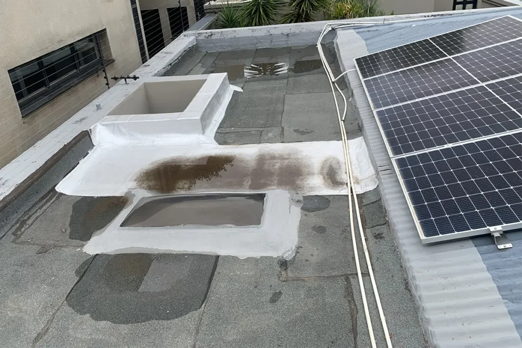 Roof waterproofing Parkhurst before image showing flat roof skylight area with water pooling and solar panels