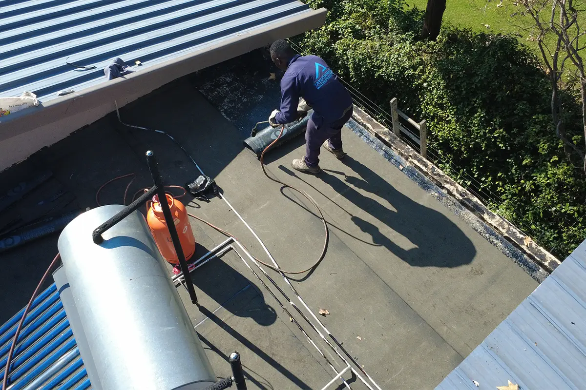 Torch-on waterproofing Randburg worker sealing membrane overlaps on a flat roof