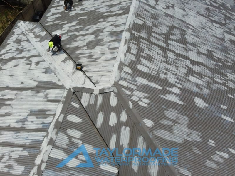 Drone close up of TM Waterproofing applying protective paint on a section of a corrugated roof.