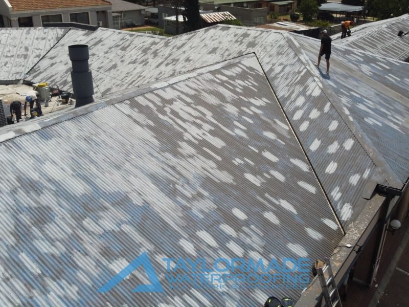 Drone view of a TM Waterproofing expert inspecting protective paint on a corrugated roof.