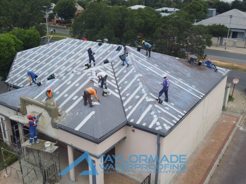Drone view of TM Waterproofing applying painting, and performing construction on a section of the corrugated roof.