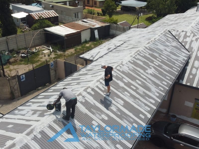 Drone view of a TM worker and expert on a corrugated roof overseeing membranes and protective paint application.