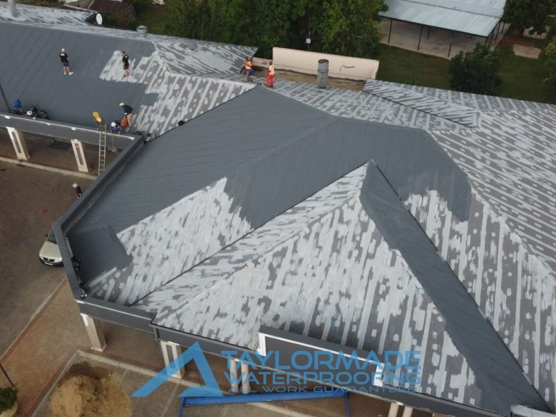 Wide aerial view of corrugated roof showing membranes applied with protective paint pending, highlighting roof work in progress.