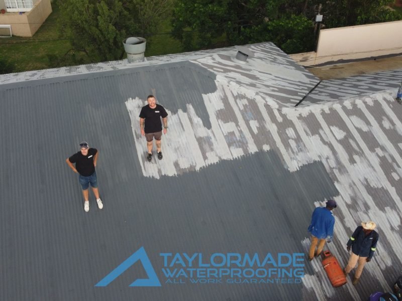 Drone view of TM workers on a corrugated roof with experts supervising the application of membranes and protective paint.