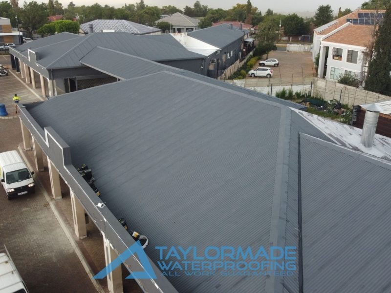 Close drone view of three connected corrugated roof sections with protective paint applied, showing detailed waterproofing coverage.