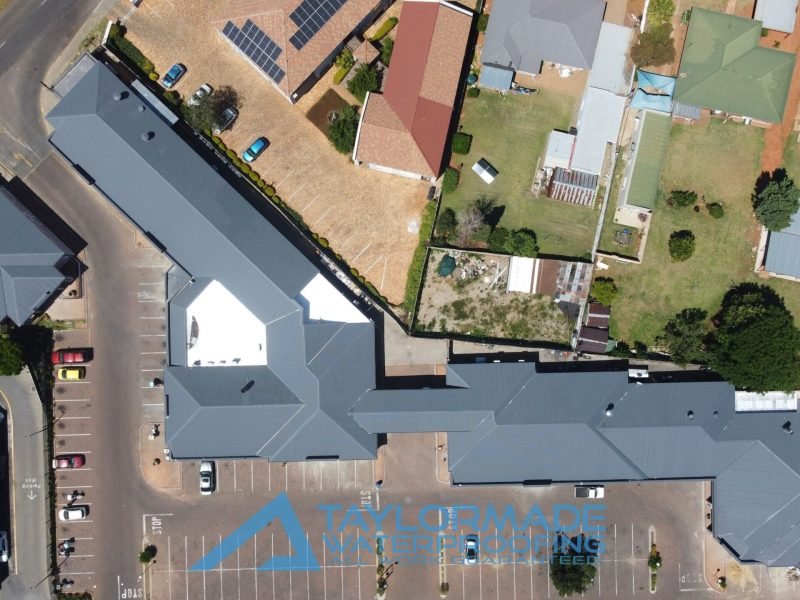 Far top drone view of connected corrugated roof sections with protective paint applied, showing full waterproofing coverage.