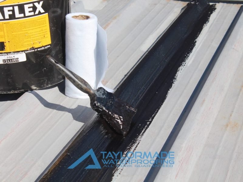 Paint brush next to bucket of acrylic waterproofing paint ready for roof application.