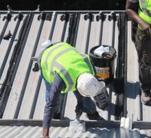 TM Waterproofing applying a protective coating on a corrugated roof for long lasting durability and weather protection.