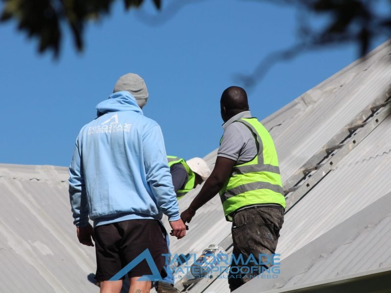 TM Waterproofing and an inspector applying acrylic waterproofing paint on a corrugated roof