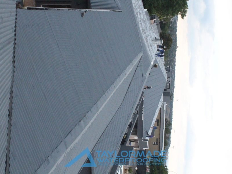 TM Waterproofing applying protective paint on a corrugated roof for enhanced durability and protection.