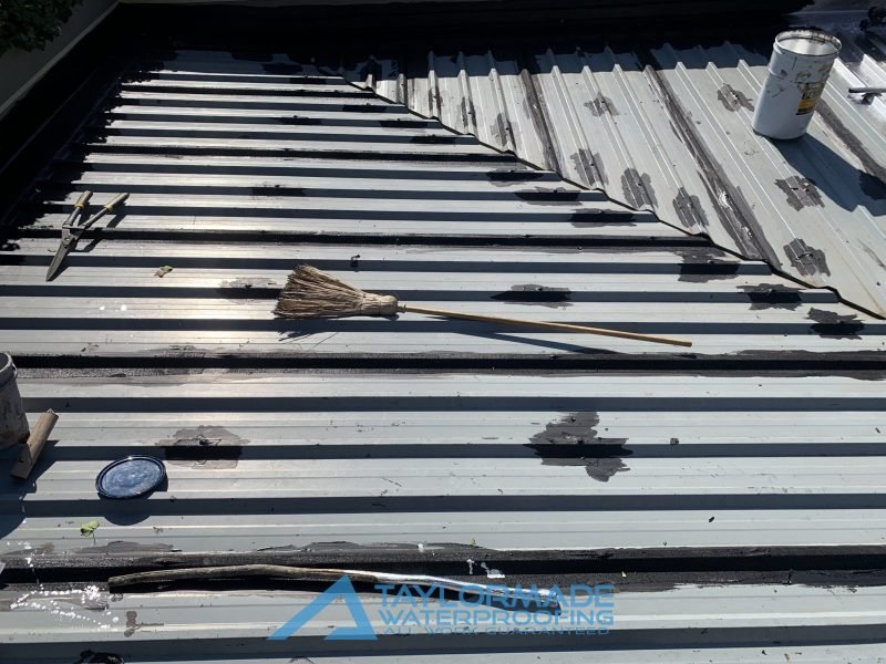 Corrugated roof in Parkhurst with protective painting applied halfway, improving durability and water resistance.