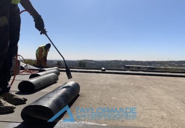 TM Waterproofing applying a torch‑on waterproofing membrane; close view of one technician holding the torch during application.