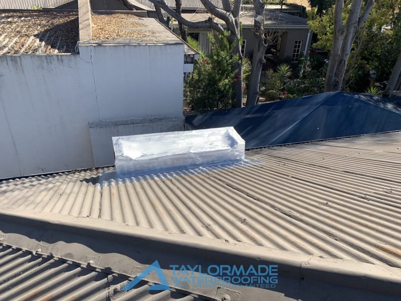 Flat roof with chimney coated in silver paint for waterproofing and UV protection.