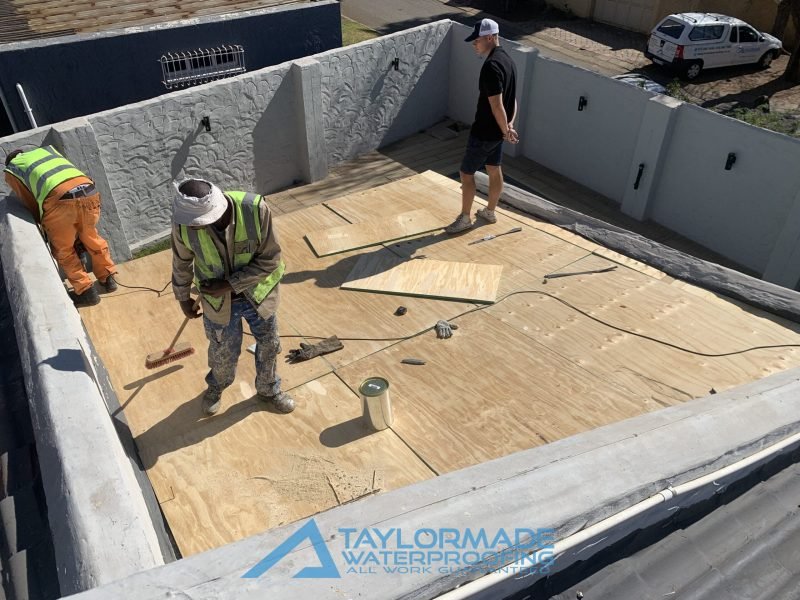 TM Waterproofing installing boards on a flat roof under the supervision of an expert, preparing for Board & Torch Waterproofing.