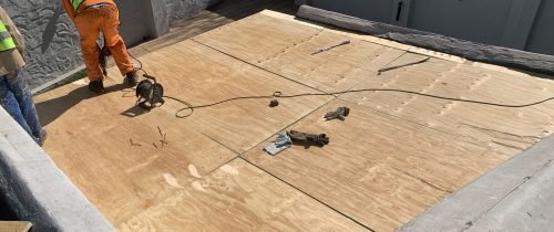 TM Waterproofing installing boards on a flat roof with drills, preparing the surface for Board & Torch Waterproofing.