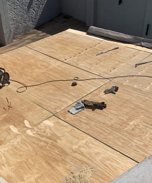 TM Waterproofing installing boards on a flat roof with drills, preparing the surface for Board & Torch Waterproofing.