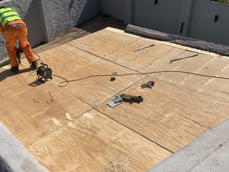 TM Waterproofing installing boards on a flat roof with drills, preparing the surface for Board & Torch Waterproofing.