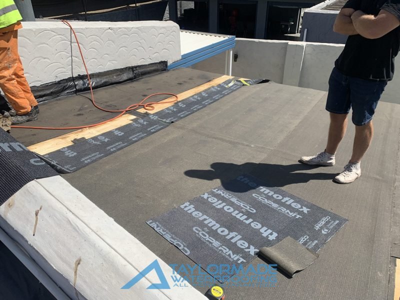 Flat roof with TM Waterproofing technicians applying Board & Torch Waterproofing, showing progress of installation.