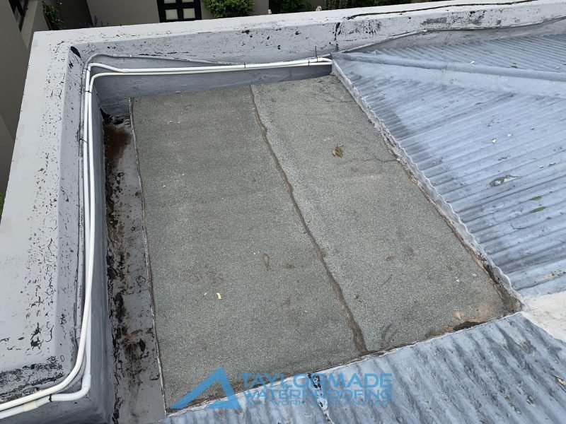 Parkhurst slab roof before waterproofing, showing water damage on the edges and an old board/carpet in the center, ready for board & torch waterproofing.